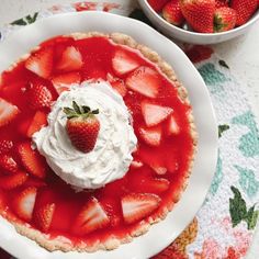 a strawberry pie with whipped cream and strawberries on the side, sitting on a floral tablecloth