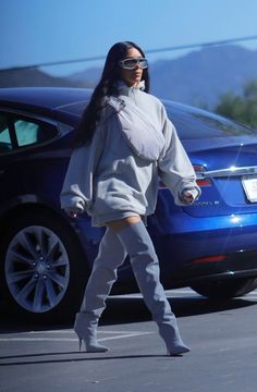 a woman walking down the street in front of a car wearing grey boots and a gray sweatshirt