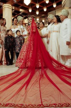 a group of people standing around a red wedding dress