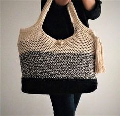 a woman carrying a black and white knitted tote bag with tassels