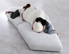 two people laying on top of a large white couch in the middle of an empty room