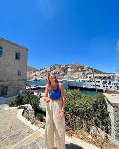 a woman standing in front of a harbor with boats on the water and buildings behind her