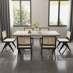 a dining room table with four chairs and a vase on the table in front of two windows