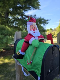 a santa clause sitting on top of a mailbox with an elf hat and green dress