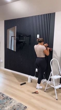 a woman standing in front of a black wall holding a paint roller and painting the walls