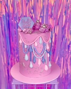 a pink cake with beads and jewels on it sitting on a stand in front of a purple background