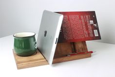 an apple laptop computer sitting on top of a wooden stand next to a green cup