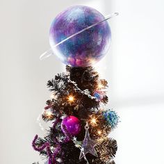 a small christmas tree with ornaments and lights on it's top, in front of a window