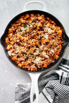 a skillet filled with meat and cheese on top of a white tablecloth next to a striped towel