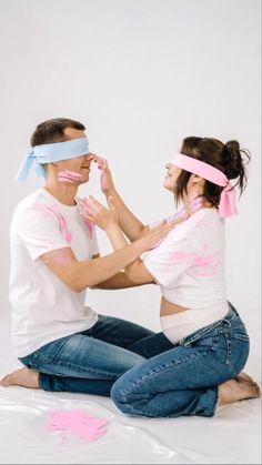 a man and woman sitting on the ground wearing blindfolds with their faces painted pink