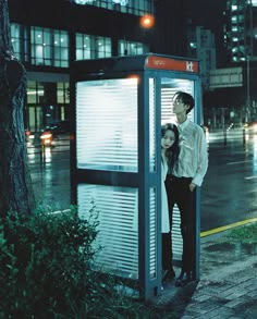 a man and woman standing in front of a phone booth on the street at night