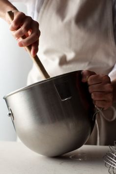 a person holding a metal bowl with a wooden spoon in it and another hand on top of the bowl