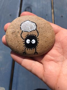 a hand holding a rock with a cartoon character painted on it