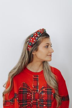 a woman with long hair wearing a red sweater and plaid bow headband, looking off to the side