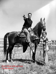 a man sitting on the back of a horse next to a little boy in a field