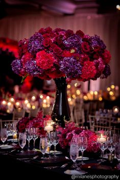 a vase filled with purple and red flowers on top of a table covered in wine glasses