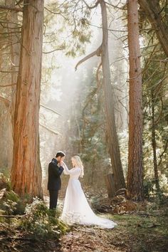 a bride and groom standing in the woods