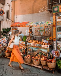 a woman walking past a fruit stand with oranges and other fruits on display in baskets