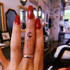 a woman's hand with a small crescent tattoo on her left ring, and a red manicure