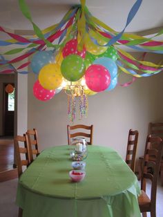 a green table topped with lots of balloons and streamers hanging from it's ceiling