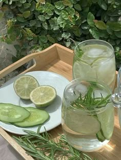 two glasses filled with water and sliced cucumbers on a tray next to some lemons