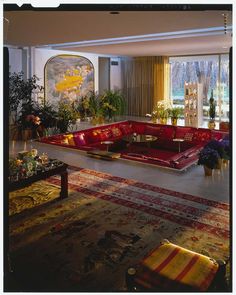 a living room filled with lots of red couches next to a large painting on the wall