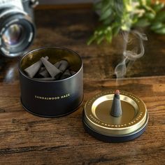 a metal container filled with matches sitting on top of a wooden table next to a camera