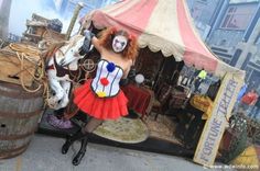 a woman dressed as a clown standing in front of a tent with a horse on it