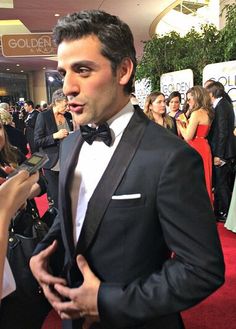 a man in a tuxedo talking to someone on the red carpet