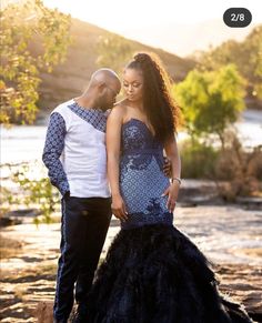 a man and woman standing next to each other in front of a river with trees