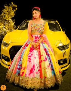 a woman standing in front of a yellow car wearing a colorful dress and headpiece