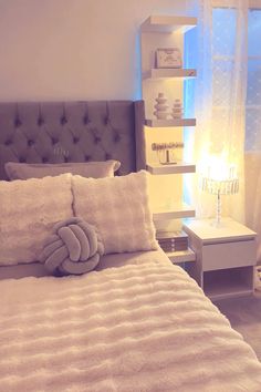 a white bed with pillows and a stuffed animal on it's head in front of a window