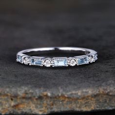 a white gold band with blue topaz and diamonds on the side, sitting on a rock