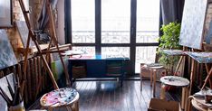 an artist's studio with lots of easels and paintings on the walls in front of a window