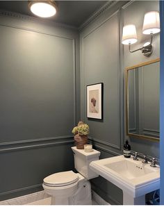 a white toilet sitting next to a sink in a bathroom under two lights on the wall