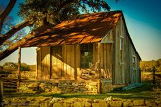 a small wooden cabin with a porch and rocking chair in the front yard, near a tree