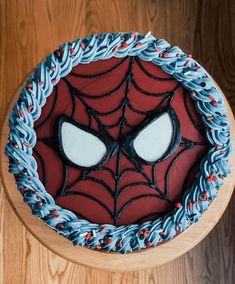 a spiderman cake with blue frosting and red icing on a wooden table