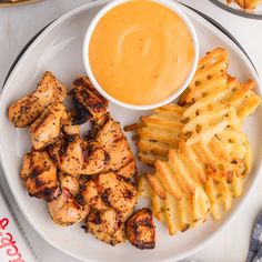 a white plate topped with chicken and french fries next to a bowl of dipping sauce