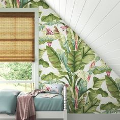 a bed sitting under a window next to a green leaf covered wallpaper in a bedroom