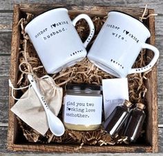 two white coffee mugs in a wooden box with spoons and other items inside