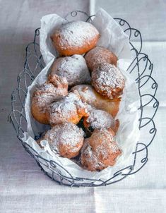 powdered doughnuts in a wire basket on a white tablecloth covered table