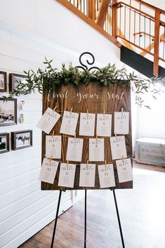 a wooden sign with seating cards attached to it and greenery on the top, in front of stairs