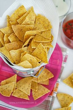 some tortilla chips are in a bowl on a pink plate with sauces