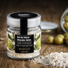 a jar filled with salt sitting on top of a wooden table next to olives