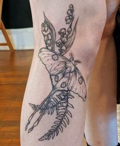 a woman's leg with a butterfly and flowers tattoo design on it, sitting on a wooden floor