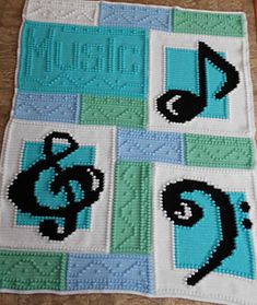 a crocheted blanket with music notes and trebles on the squares in blue, green, and white