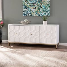 a white cabinet sitting on top of a wooden floor next to a vase filled with flowers