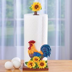 a white toilet paper holder with sunflowers and a rooster on it next to eggs