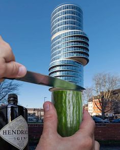 a person is holding a cucumber in front of a building with a large knife