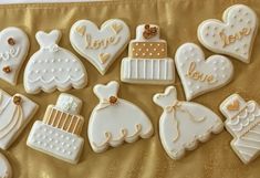 decorated cookies in the shape of wedding gowns and cakes on a gold tablecloth